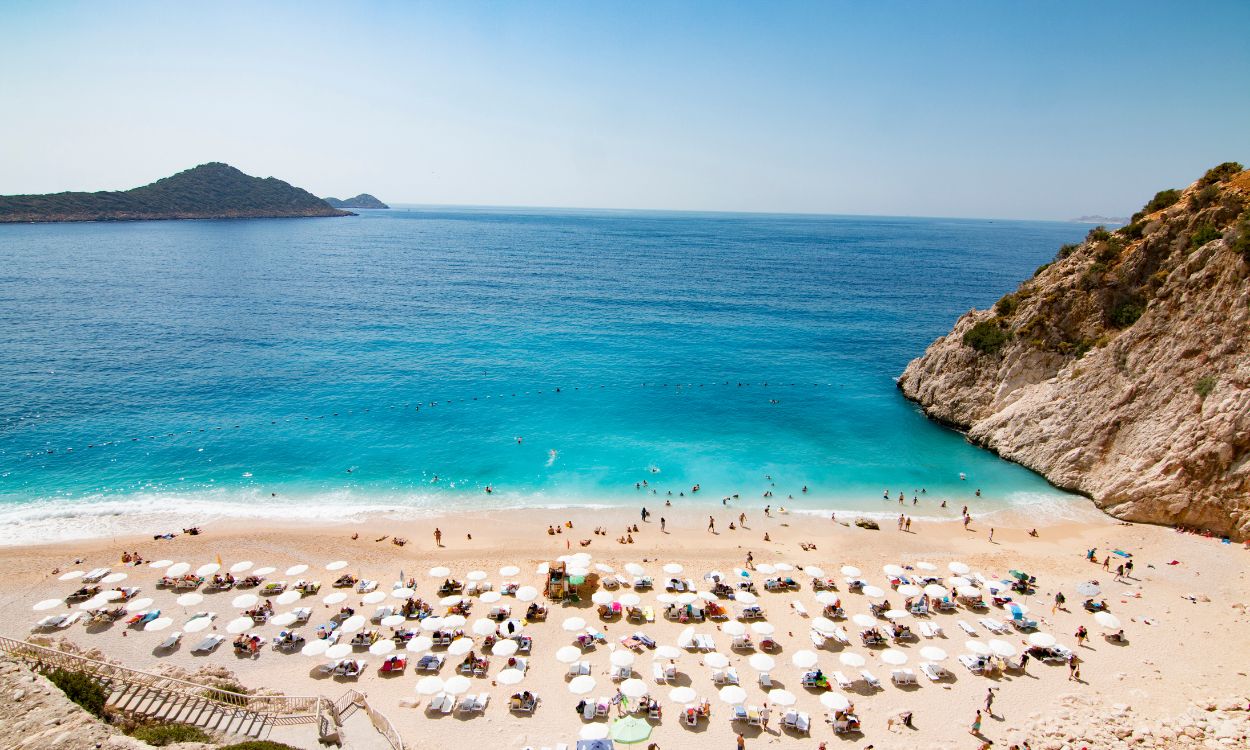 Mala-Strand in der Türkei: Eine Bucht mit türkisblauem Meer, felsiger Steilküste und hellem Sandstrand voller weißer Sonnenschirme. Mala-Strand in der Türkei: Eine Bucht mit türkisblauem Meer, felsiger Steilküste und hellem Sandstrand voller weißer Sonnenschirme.