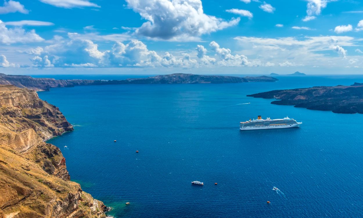 Großes Kreuzfahrtschiff in einer tiefblauen Meeresbucht bei Santorin, umgeben von steilen, braunen Felsküsten unter leicht bewölktem Himmel. Großes Kreuzfahrtschiff in einer tiefblauen Meeresbucht bei Santorin, umgeben von steilen, braunen Felsküsten unter leicht bewölktem Himmel.