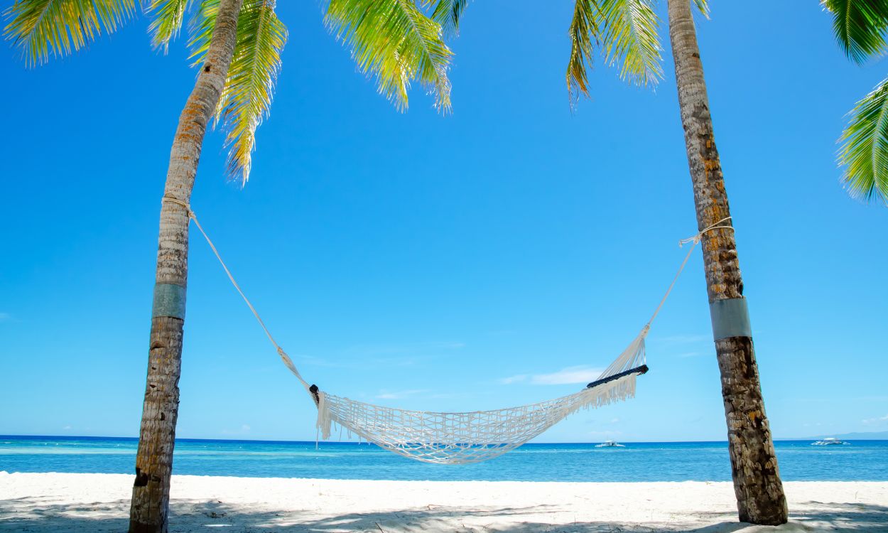 Netzhängematte zwischen zwei Palmen an einem weißen Sandstrand vor türkisblauem Meer und klarem, blauem Himmel. Netzhängematte zwischen zwei Palmen an einem weißen Sandstrand vor türkisblauem Meer und klarem, blauem Himmel.